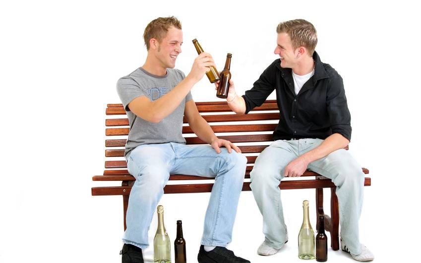 Zwei Männer sitzen auf einer Bank und stoßen mit Bierflaschen an.