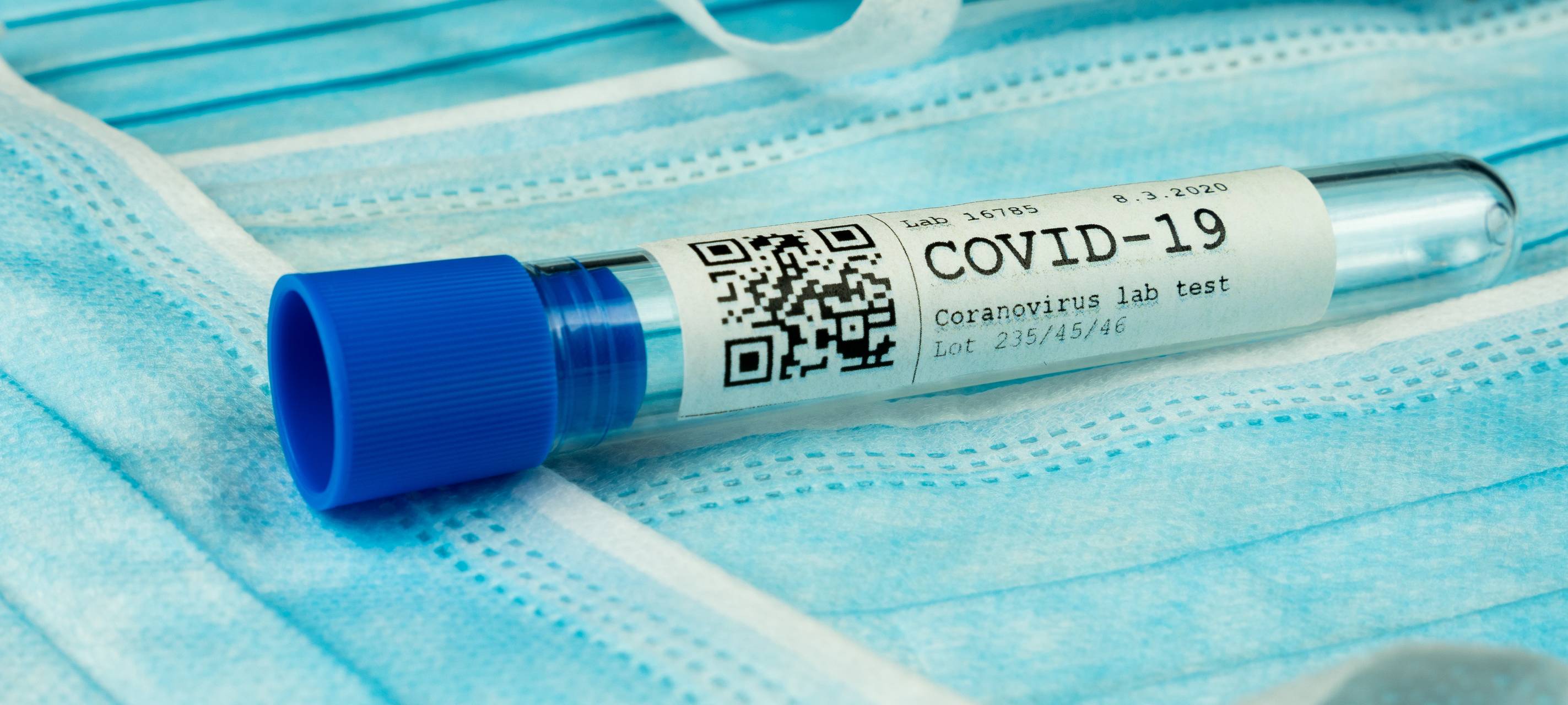 Ein Labortest-Röhrchen mit der Beschriftung COVID-19 Coronavirus Labortest liegt auf Schutzmasken.