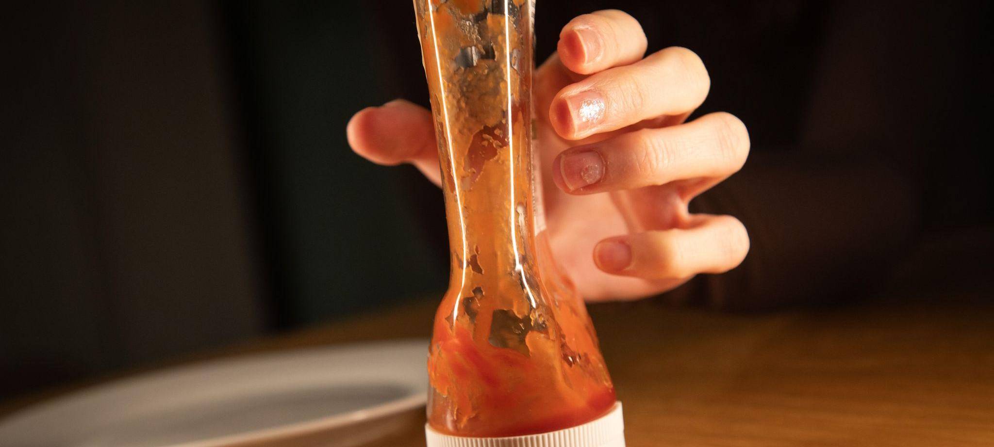 Frau greift nach einer fast leeren Ketchup-Flasche